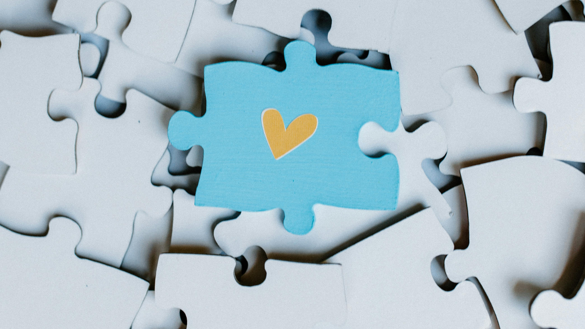 Bedürfnis oder Bedürftigkeit: Ein hellblaues Puzzleteil mit gelbem Herz auf vielen weißen Puzzleteilen.