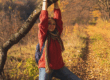 Frau mit rotem Hemd, Jeans und Rucksack häng an einem dicken Ast in herbstlichem Wald und Wiesen Ambiente